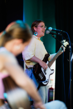 docent Simone zingt terwijl ze basgitaar speelt. Op de voorgrond speelt een leerling met haar mee.
